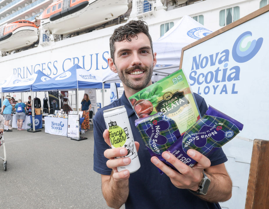 A man holding Nova Scotia Loyal products and a Nova Scotia Loyal banner in the background