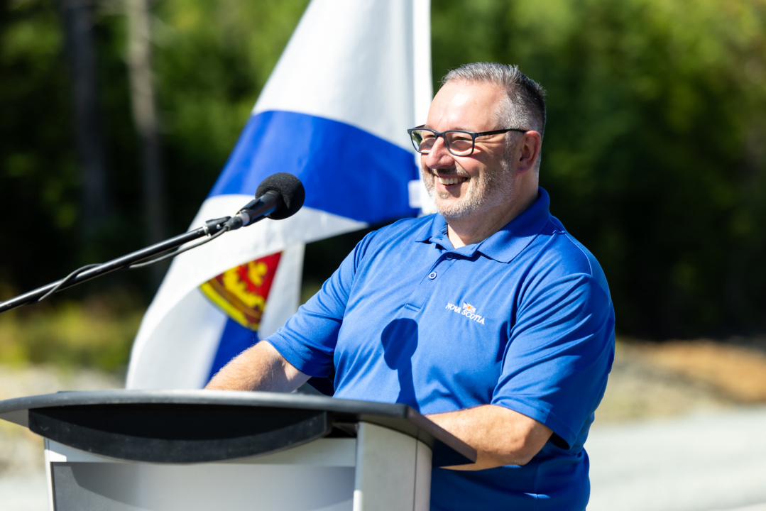 Minister of Public Works, Fred Tilley, speaks at a podium with a Nova Scotia flag in the background.