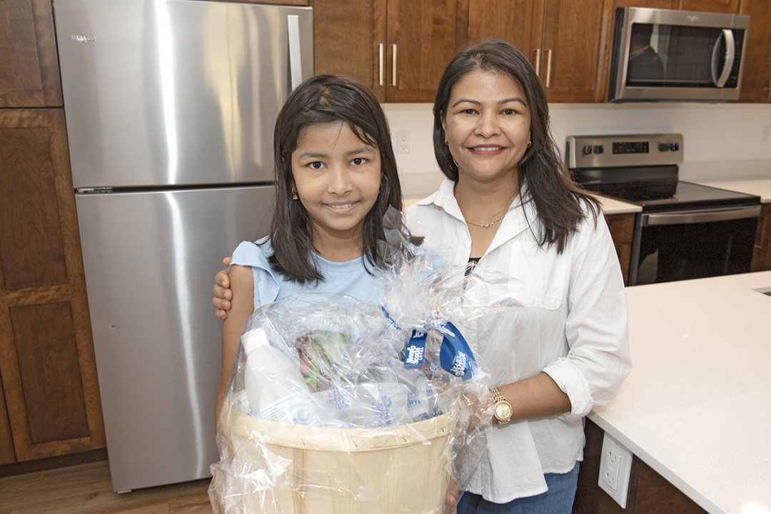 Two residents stand in their new kitchen with a basket given as a welcome present.