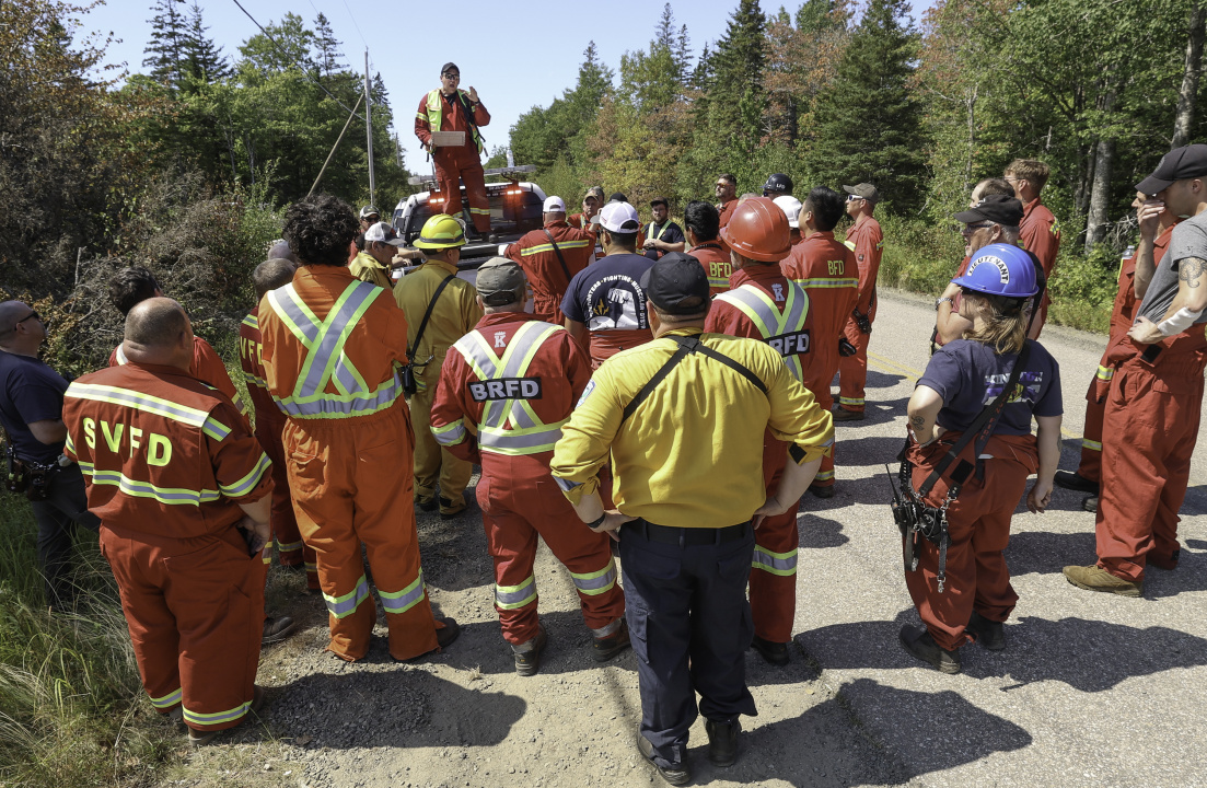 Justin Oliver, of the Bridgetown Volunteer Fire Department, stands on a truck to brief local firefighters before they begin their work.