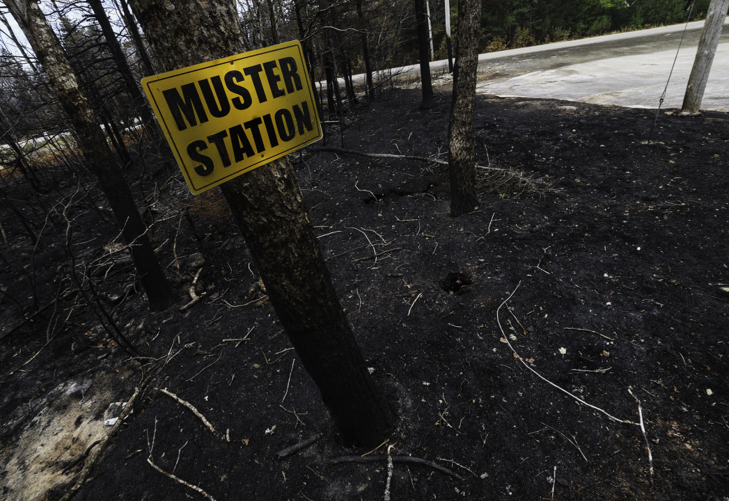 A muster station sign, charred by fire, stands in a burnt area near the West Dalhousie Community Centre