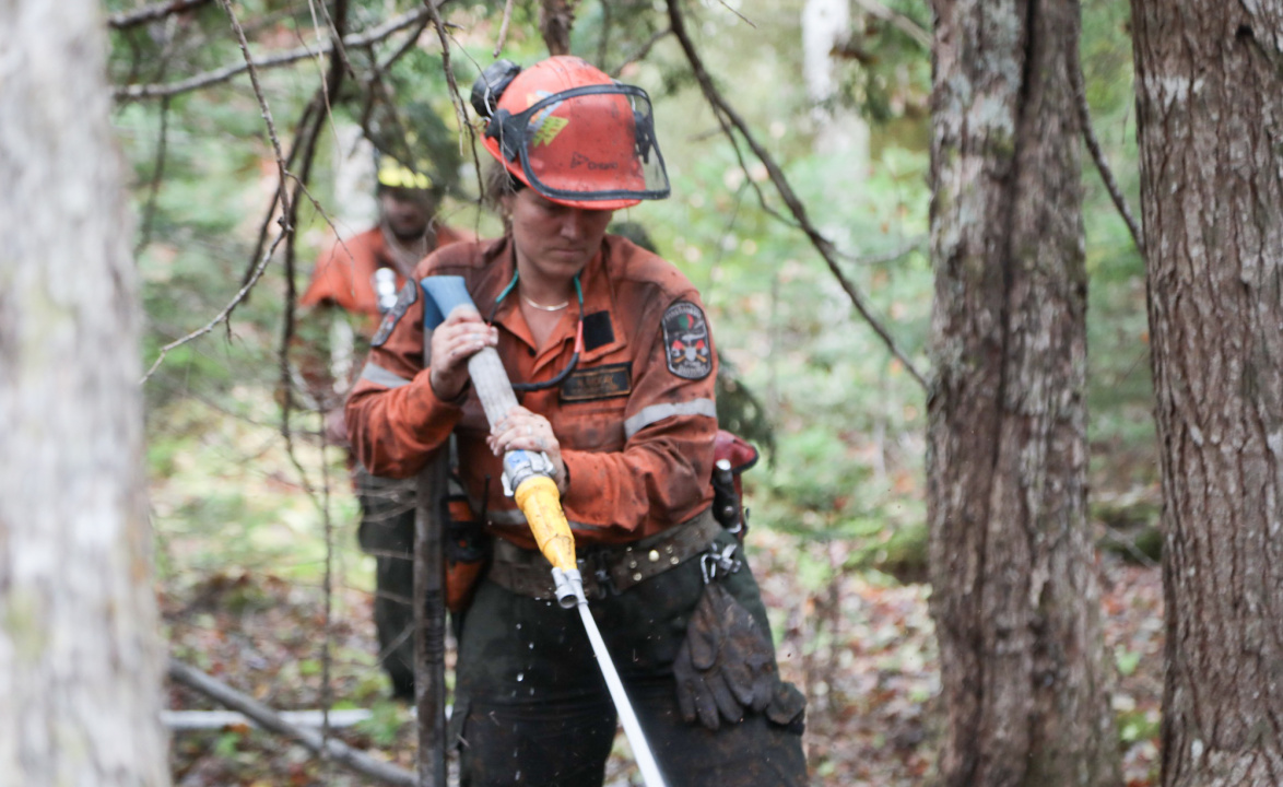 Ontario Crew Leader Neve McKay hoses down soil and smouldering tree roots at Paradise Lake.