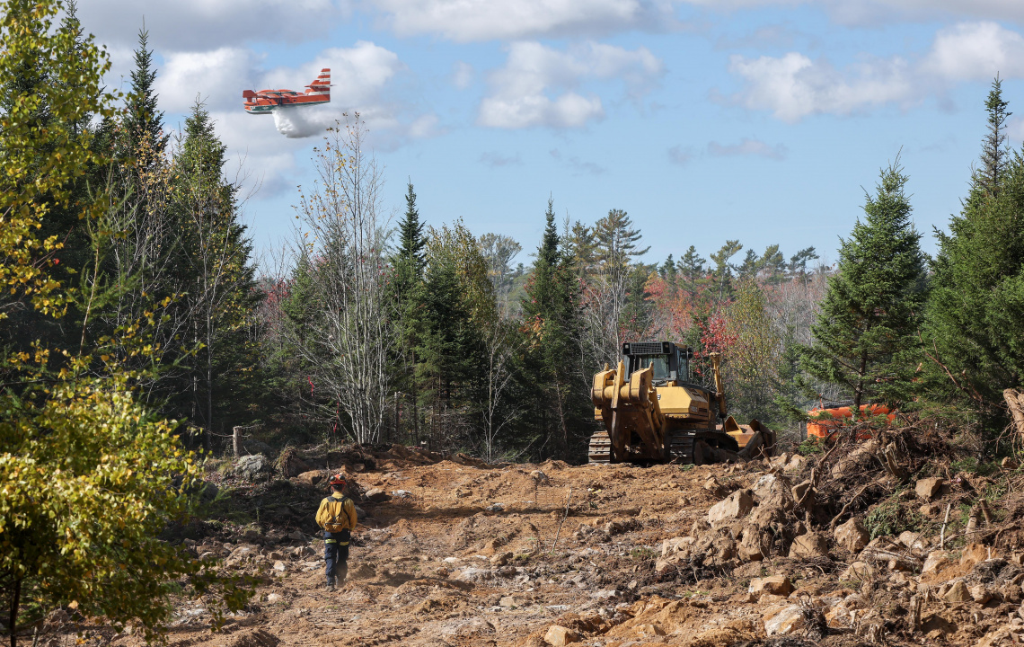 firefighters walks up a newly built fire break while a Newfoundland plane drops a load of water on the Lake George wildfire