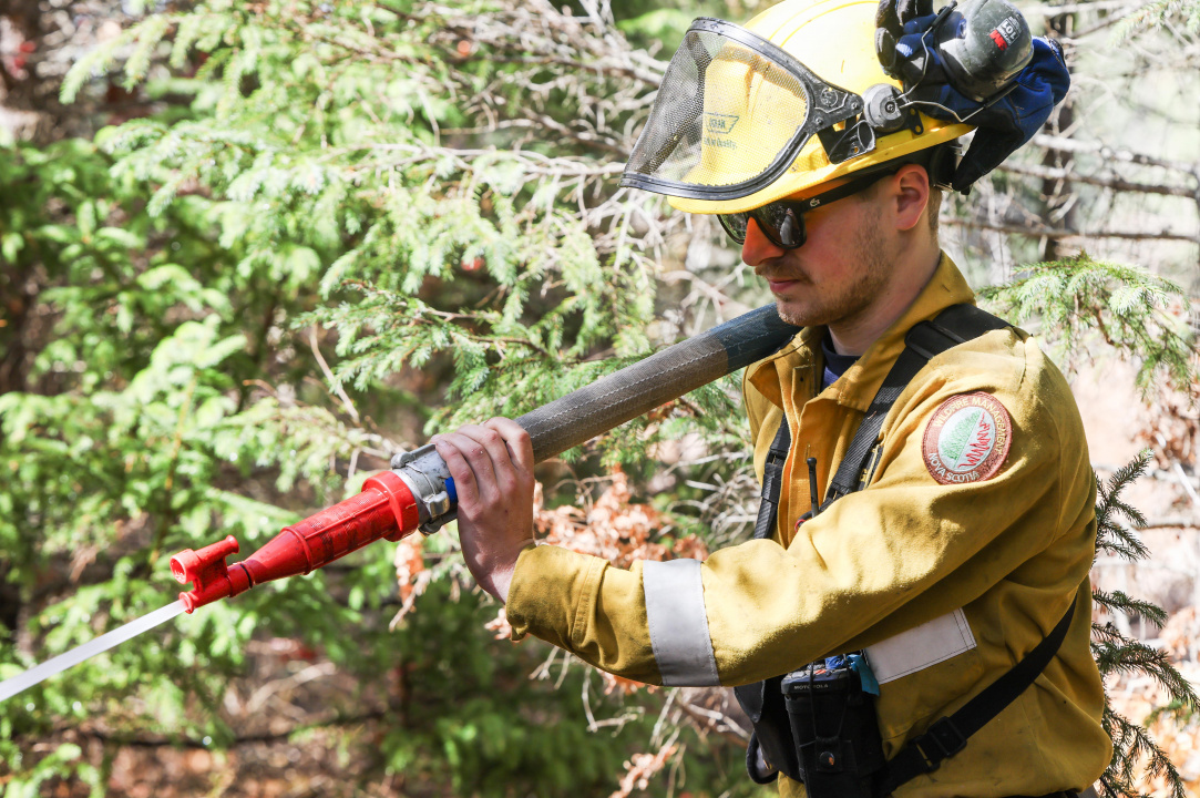 A firefighter with a hose over his shoulder spraying water on a wildfire