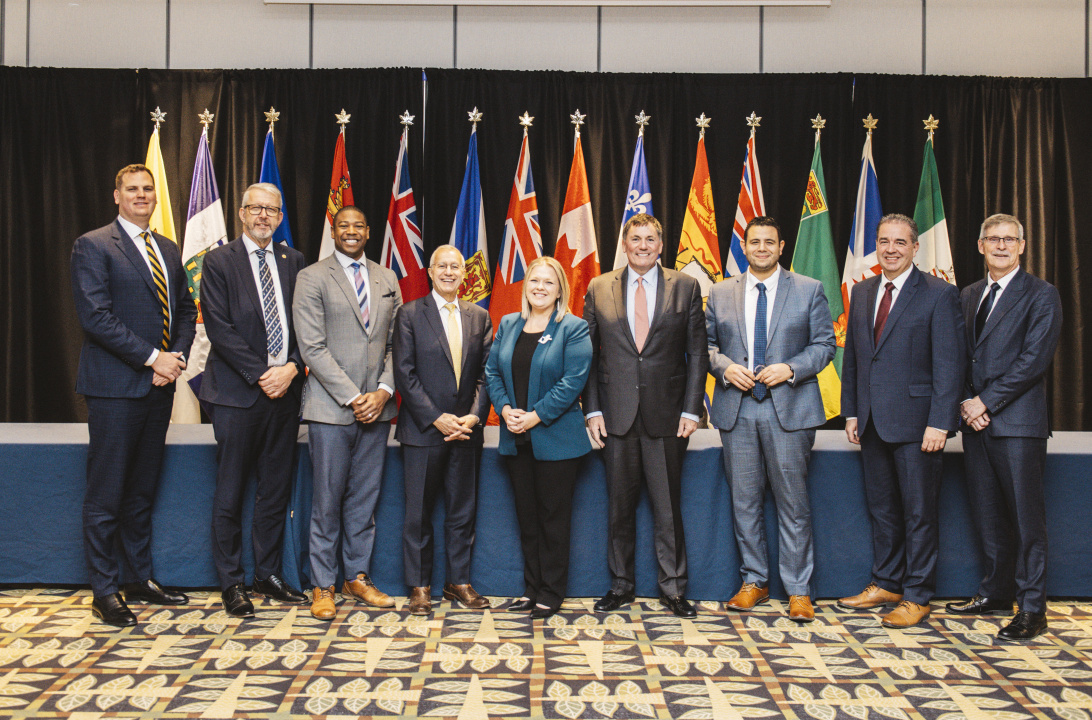 Federal and provincial ministers pose for a photo in front of flags