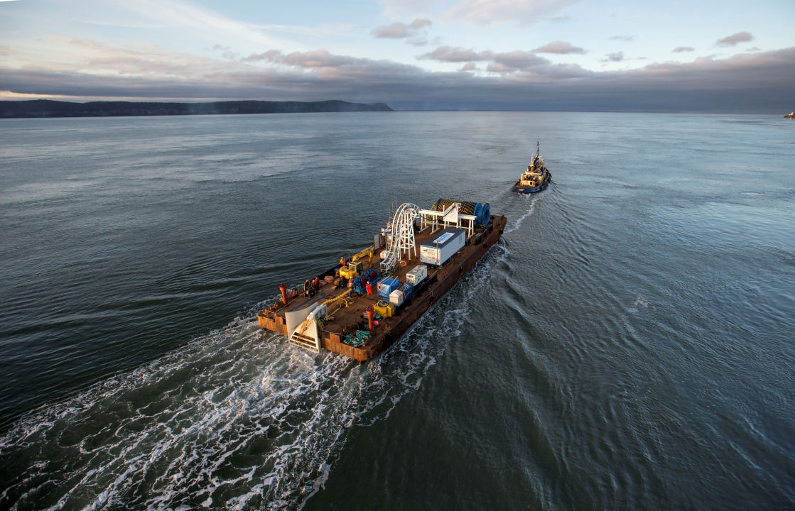 Aerial photo of a tugboat pulling a barge with equipment on it