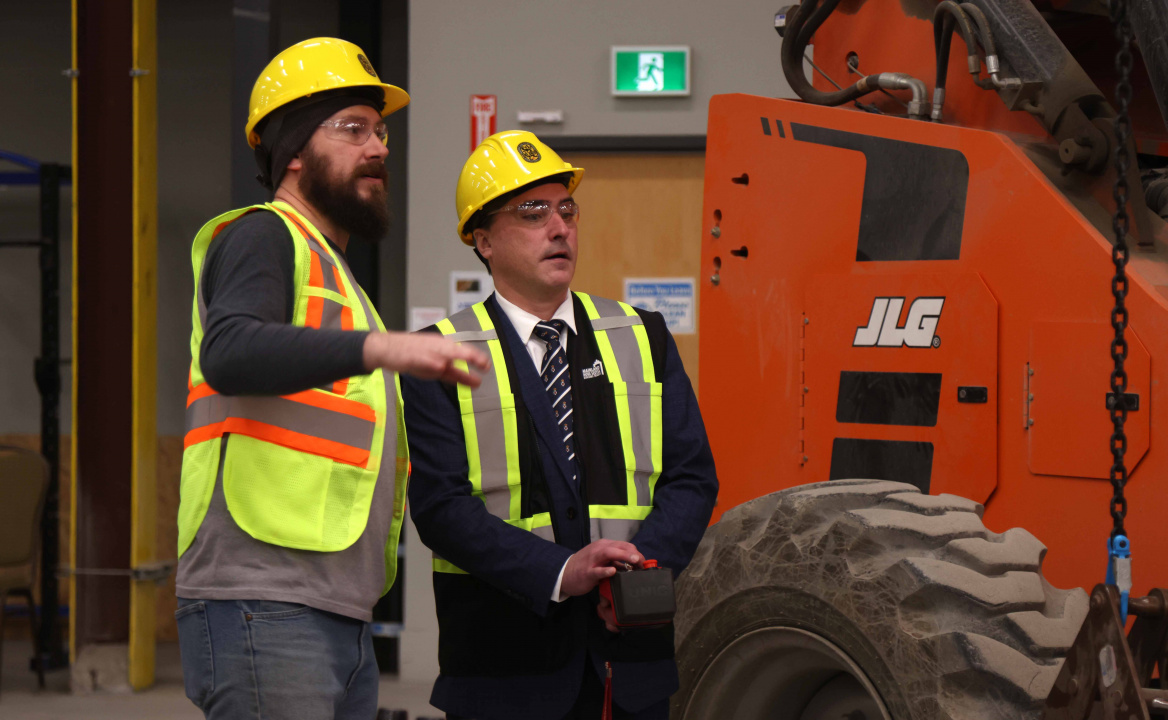 Chris Bullman, a Red Seal-endorsed Safety and Glazing Instructor, speaks with Nolan Young, Minister of Labour, Skills and Immigration, as the Minister operates a spyder lift.