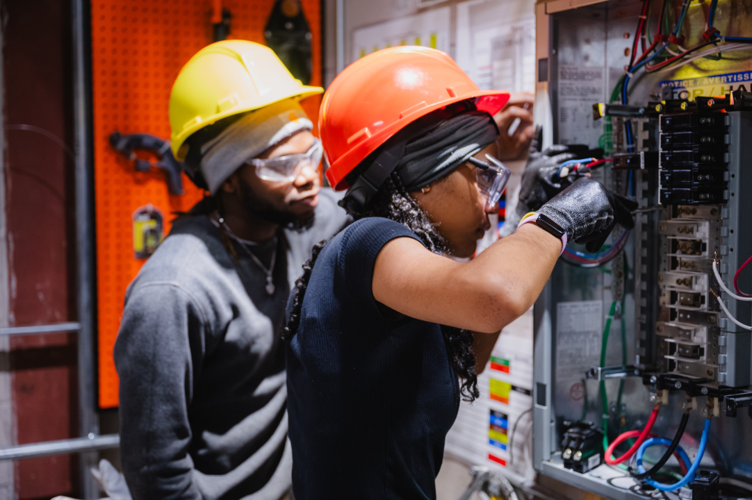 Two young African Nova Scotians  wearing hard hats do simulation work at the Trades Exhibition Hall in Halifax