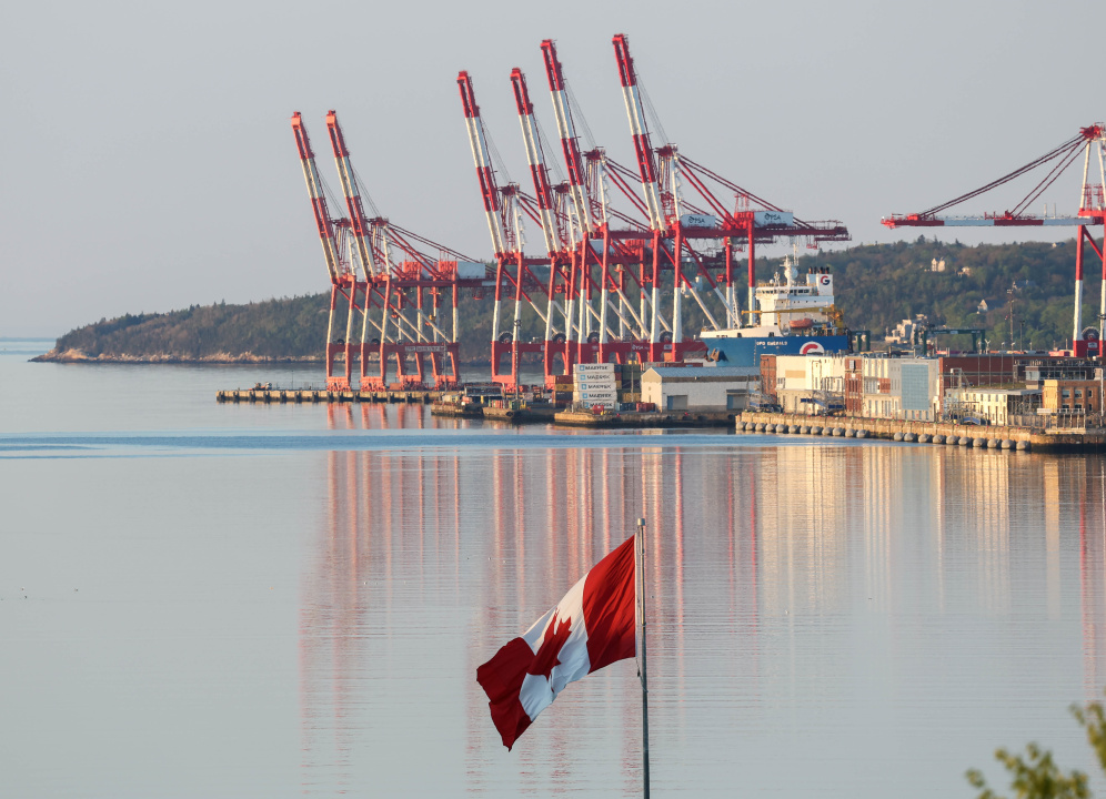 The Canadian flag in the foreground and cranes at the Port of Halifax in the background
