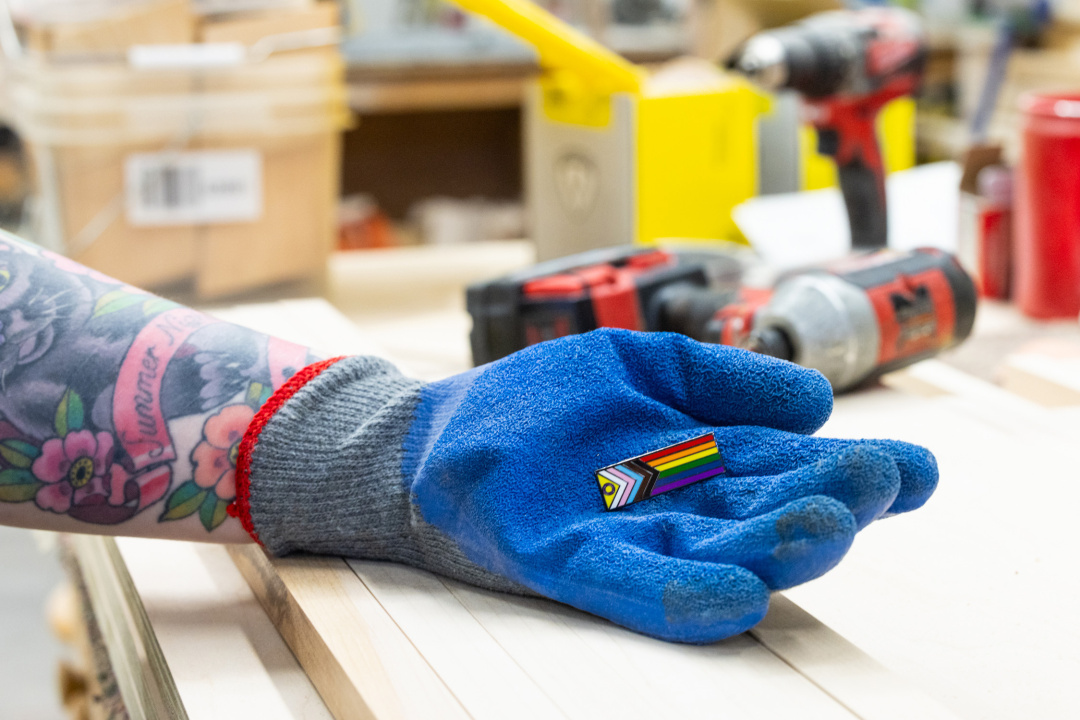 A Pride flag pin in a person's gloved hand