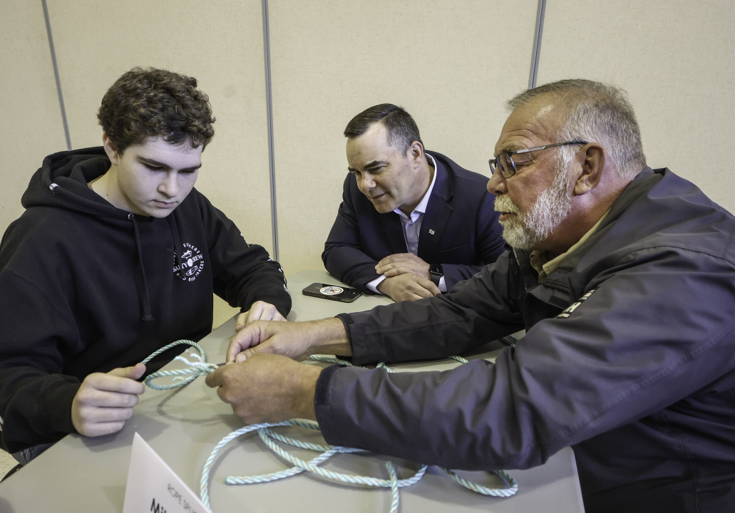 Kent Smith, Minister of Fisheries and Aquaculture (centre), watches fishing boat captain Mike Holmes show student Brayden Bower how to splice rope. 