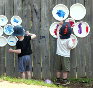 Two toddlers with hand-painted paper plates on a fence