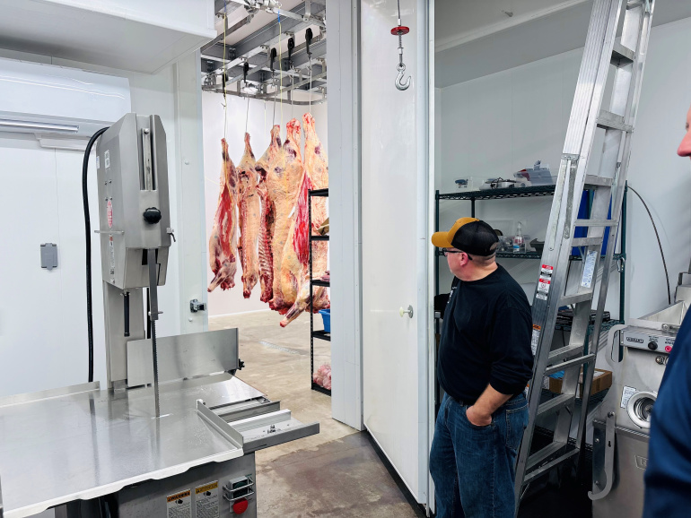 Meat hanging from hooks and a person giving a tour 